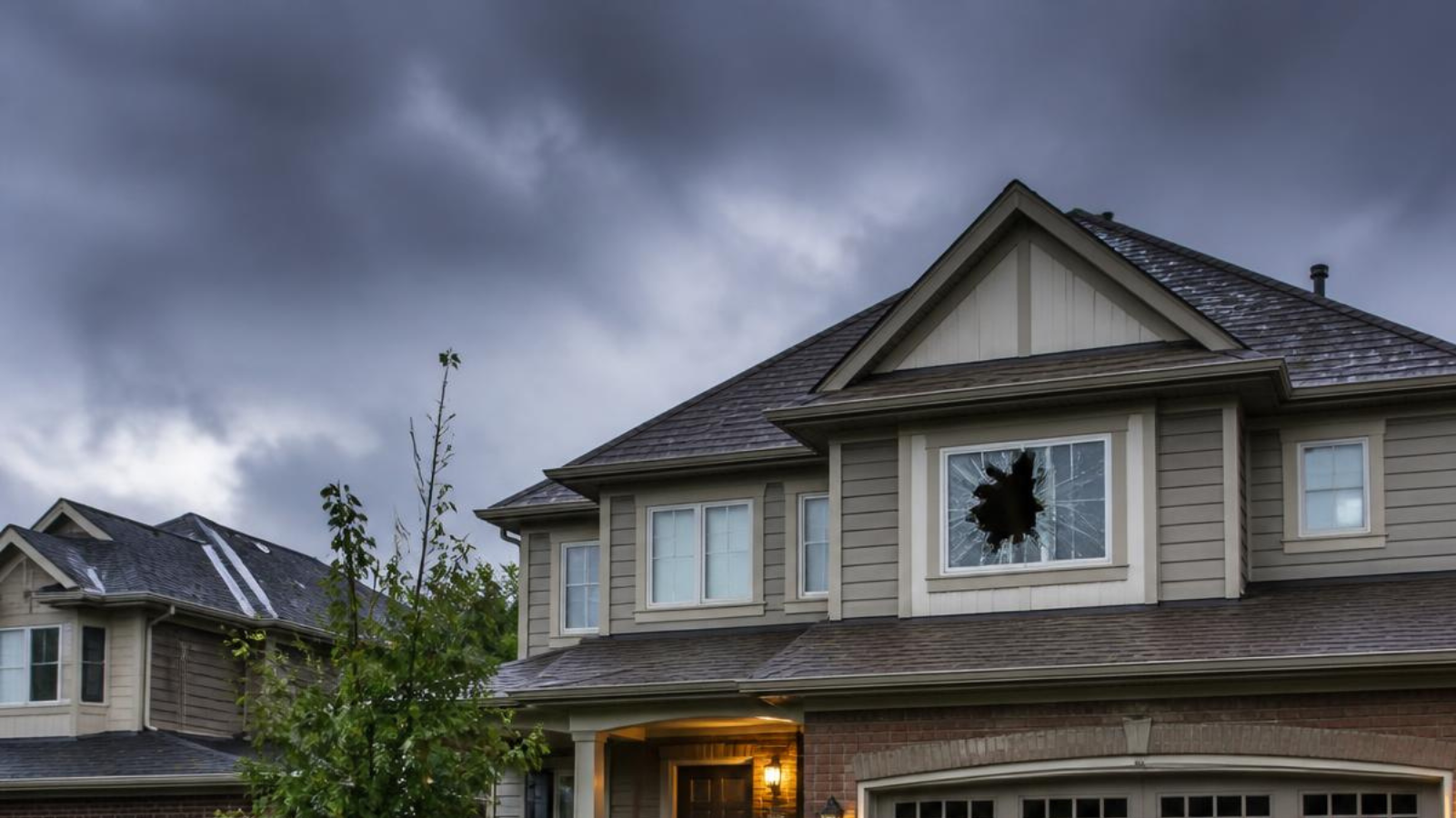 Board up window service GTA - storm-damaged home with a shattered second-floor window under dark storm clouds